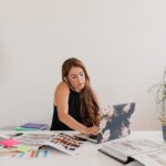 Жена говори по телефона и работи на лаптоп сред разпилени материали